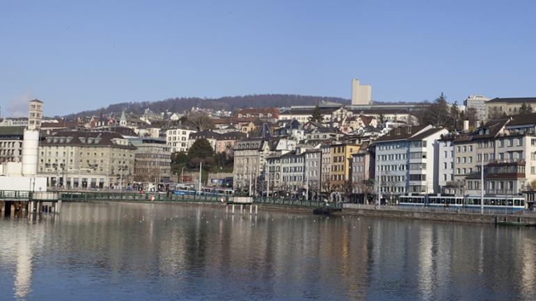 Foto von Zürich mit dem Zürichsee im Vordergrund. Dahinterliegend die Stadt.