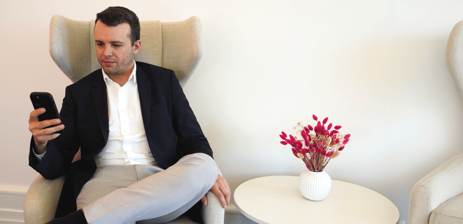 Man in business attire sitting in a lounge chair looking at his smartphone