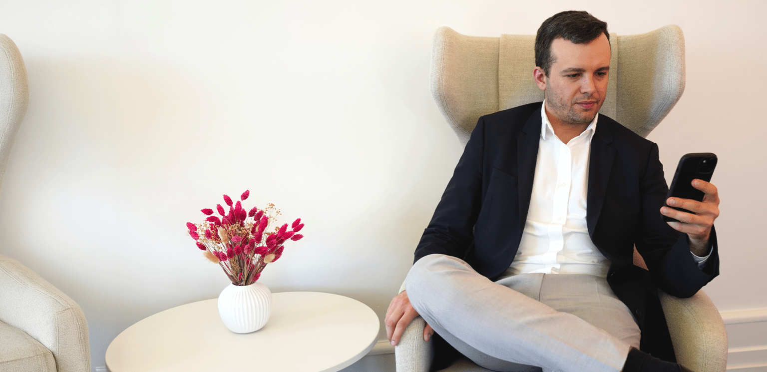 Man in business attire sitting in a lounge chair looking at his smartphone