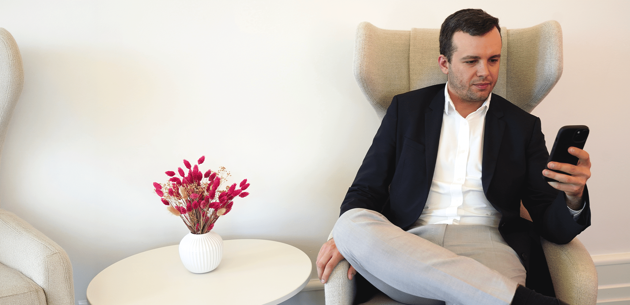Man in business attire sitting in a lounge chair looking at his smartphone