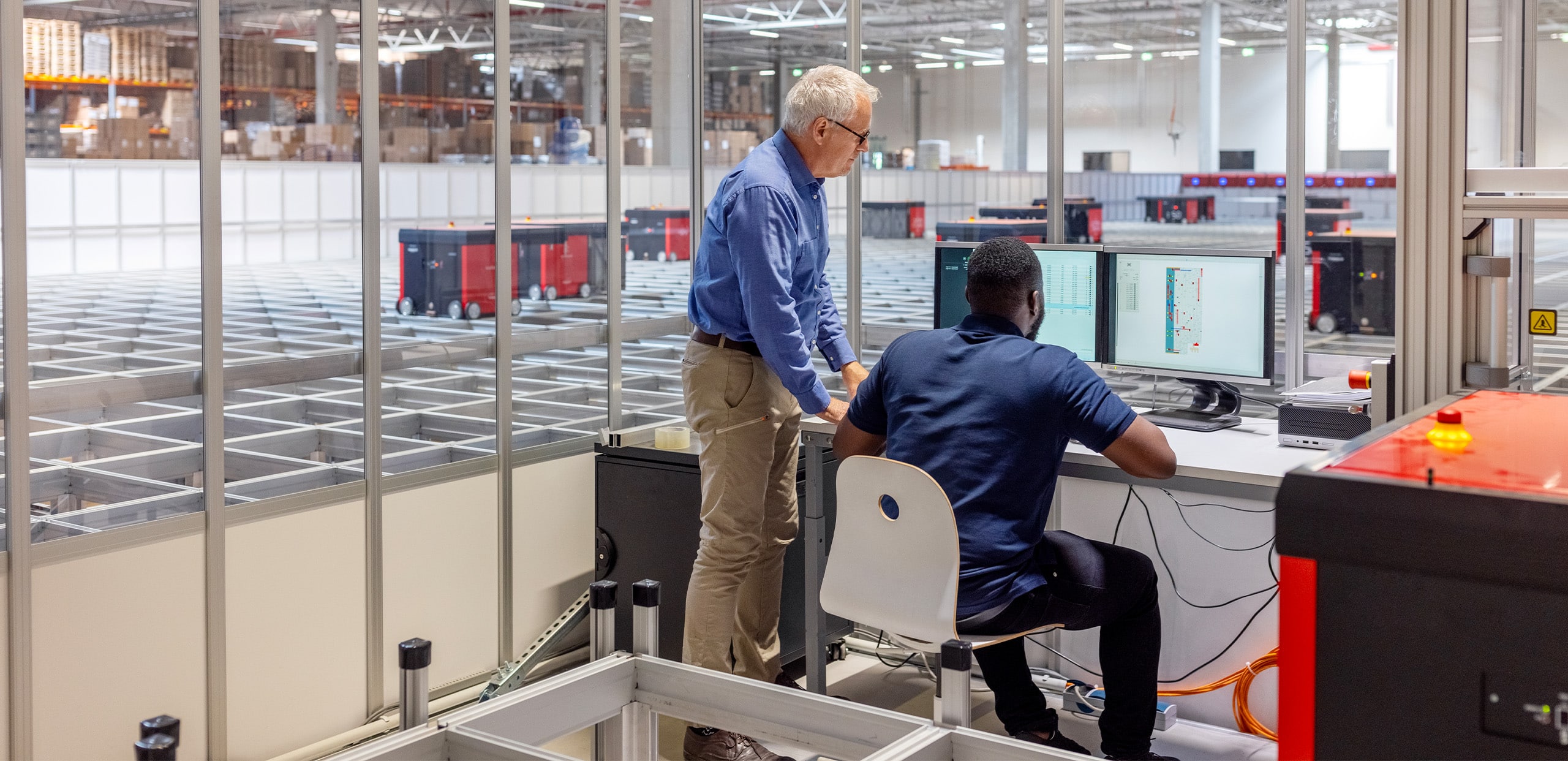 Consultants analyzing automated guided vehicle data on-screen, with a robotic warehouse system in the background.