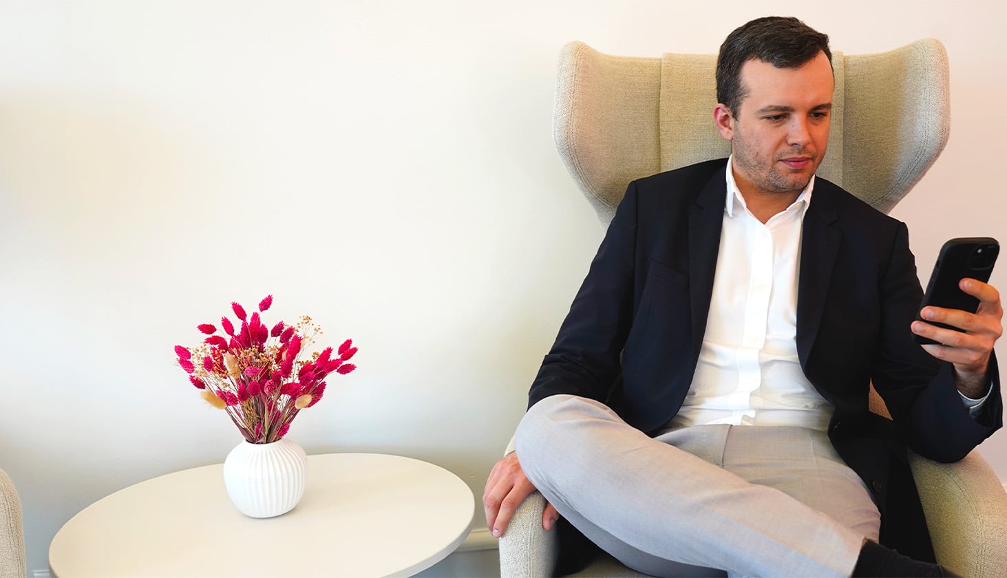 Man in business attire sitting in a lounge chair looking at his smartphone