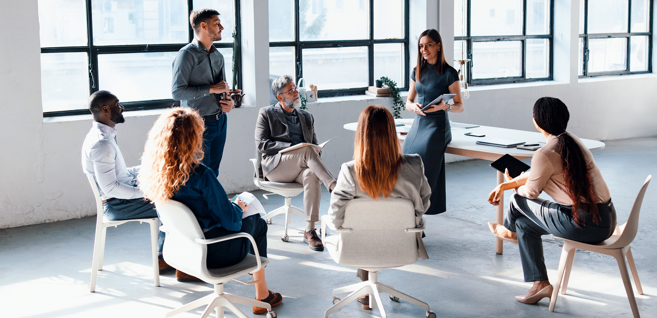 Detecon experts conducting an IREB training session, engaging with participants seated in a collaborative discussion circle in a modern office setting.